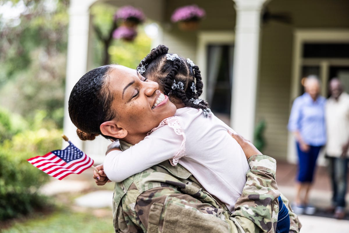 daughter embracing female us soldier mother in front of home