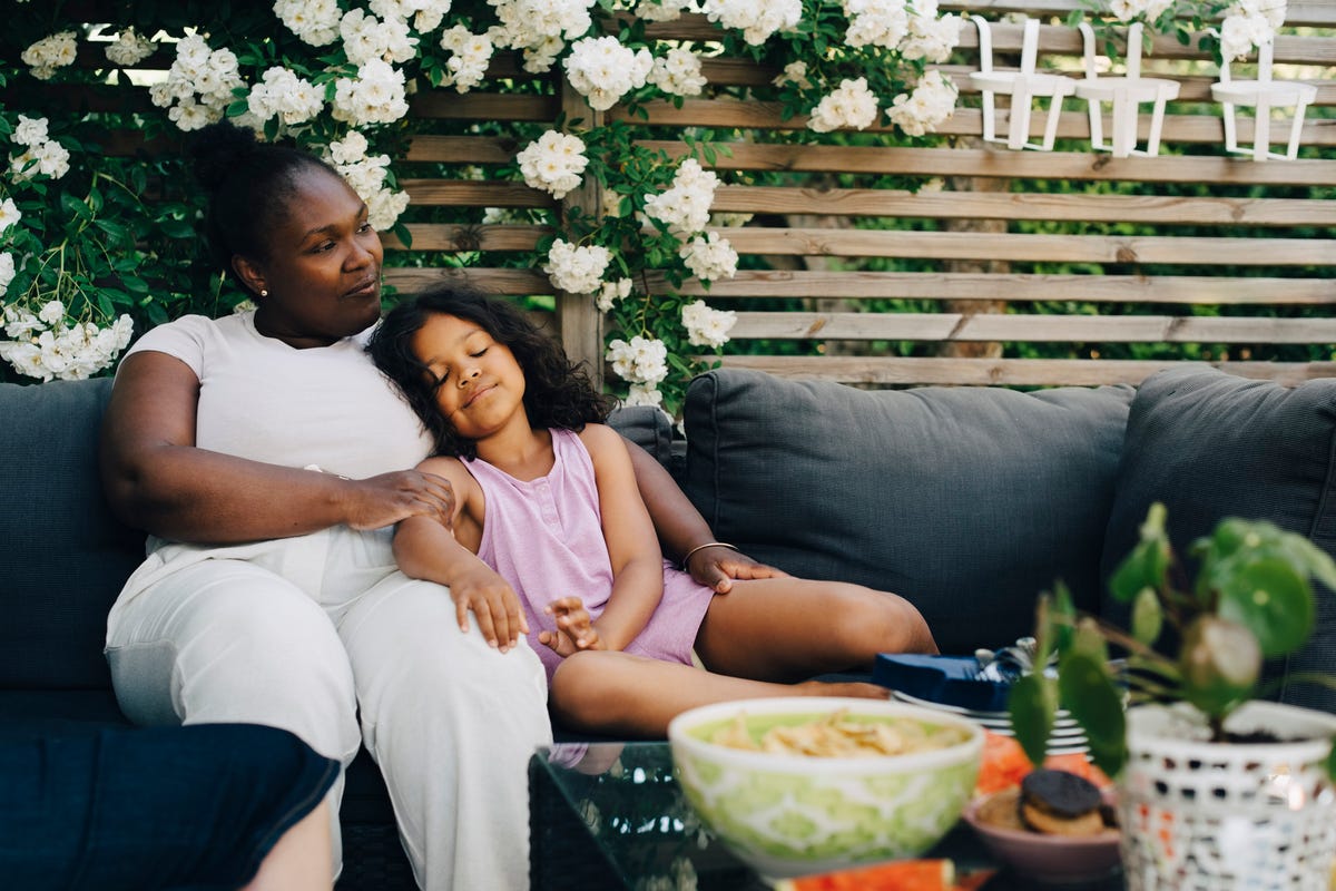 daughter resting by mother at backyard during garden party