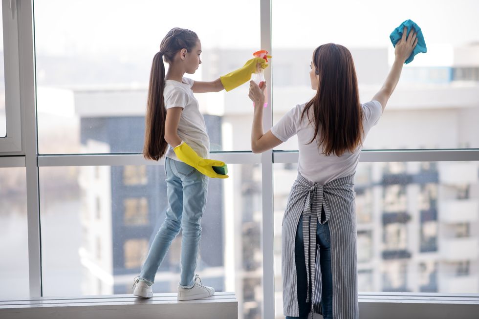 daughter standing on the windowsill and mom washing window.
