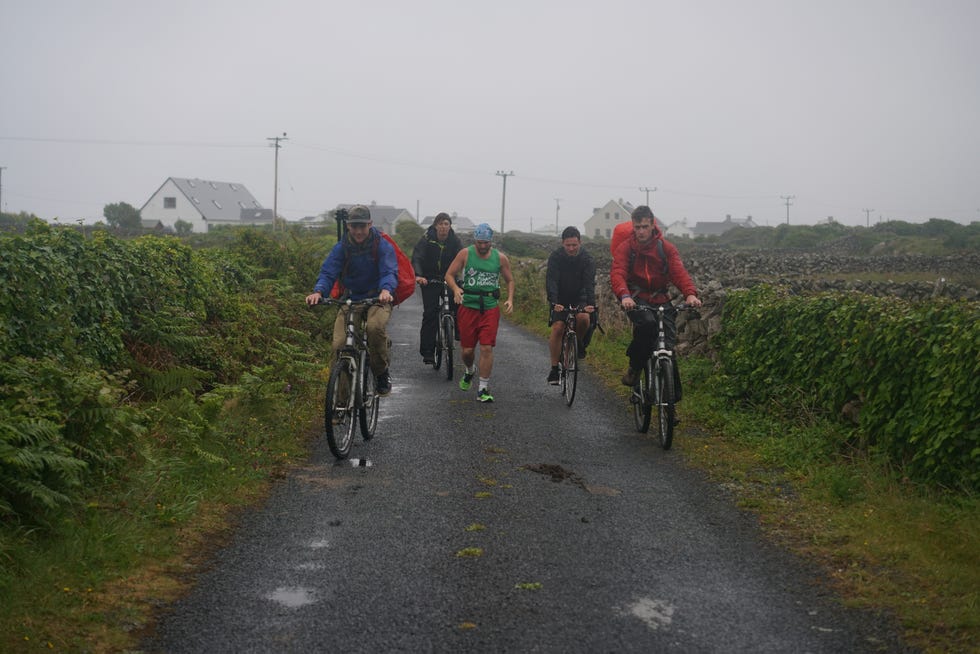 The crew of Dave Goes West rides bikes alongside Dave in the rain.
