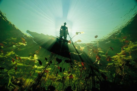 Een Bosjesman kijkt in het smaragdgroene water van de Okavango een rivier in Botswana In deze door droogte geteisterde regio is de seizoengevoelige waterstroom die wordt veroorzaakt door neerslag in Angola zon 800 kilometer verderop niets minder dan een wonder Fotograaf David Doubilet legde in 2004 voor het magazine de rijke biodiversiteit van de regio vast waar onder meer buffels krokodillen meervalachtigen en watertorren voorkomen In het jaar erna startte de National Geographic Society een project om dit water dat letterlijk van levensbelang is te beschermen