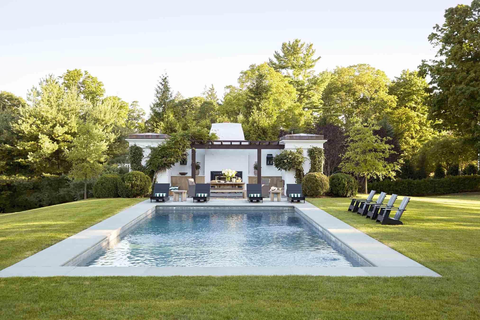 a rectangular pool inset into a lush lawn with a white california style poorhouse int he background