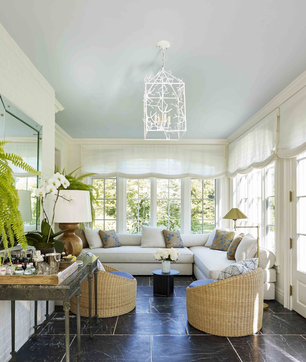 a sunroom with tall banks of windows and stone flooring and a blue ceiling with a sofa and pair of rattan chairs