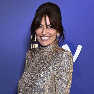 davina mccall, a woman stands smiling at the camera, she has dark hair worn up with a fringe, she wears a short silver sequin dress with long sleeves