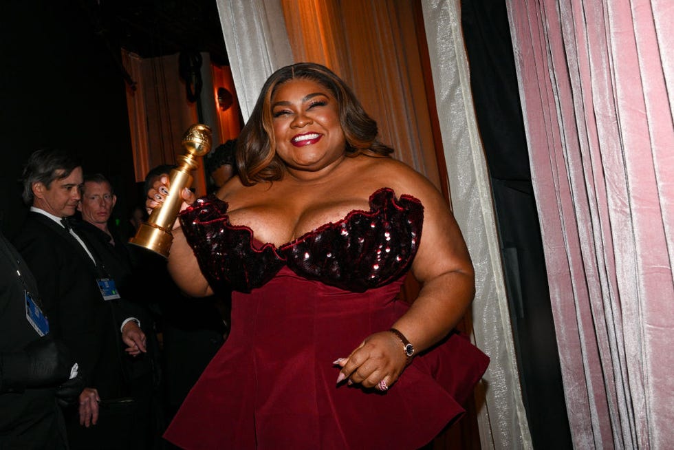 davine joy randolph smiles and holds a golden globe trophy in one hand in a backstage photo, she wears a red strapless gown with a sequin detail bust