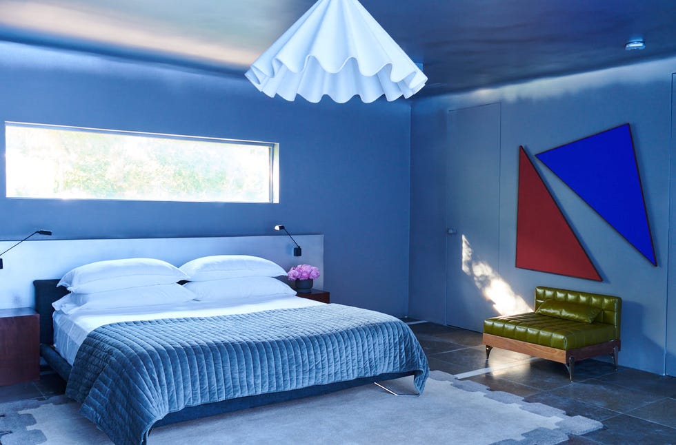 Modern bedroom featuring a bed, textured blanket, distinct artwork, and a seating area.
