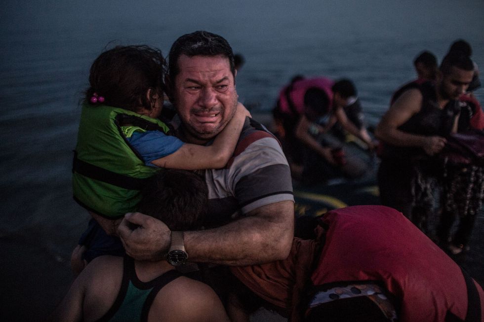 Laith Majid een Irakese vluchteling uit Bagdad barst uit in tranen van geluk en houdt zijn zoon Taha en dochter Nour in zijn armen terwijl ze veilig aankomen op een strand van het Griekse eiland Kos op 15 augustus 2015 De groep maakte de oversteek van uit de Turkse badplaats Bodrum Onderweg liep hun flinterdunne rubberboot leeg volgepropt met ongeveer 12 mannen vrouwen en kinderen