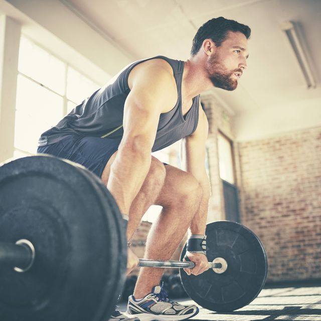 full length of confident man dead lifting barbell in gym determined fit male is looking away while exercising he is in sports wear