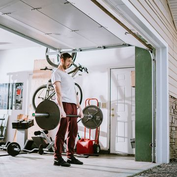 a mid adult man lifts weights in his home garage part of a regular routine, or the new normal with social distancing and covid 19