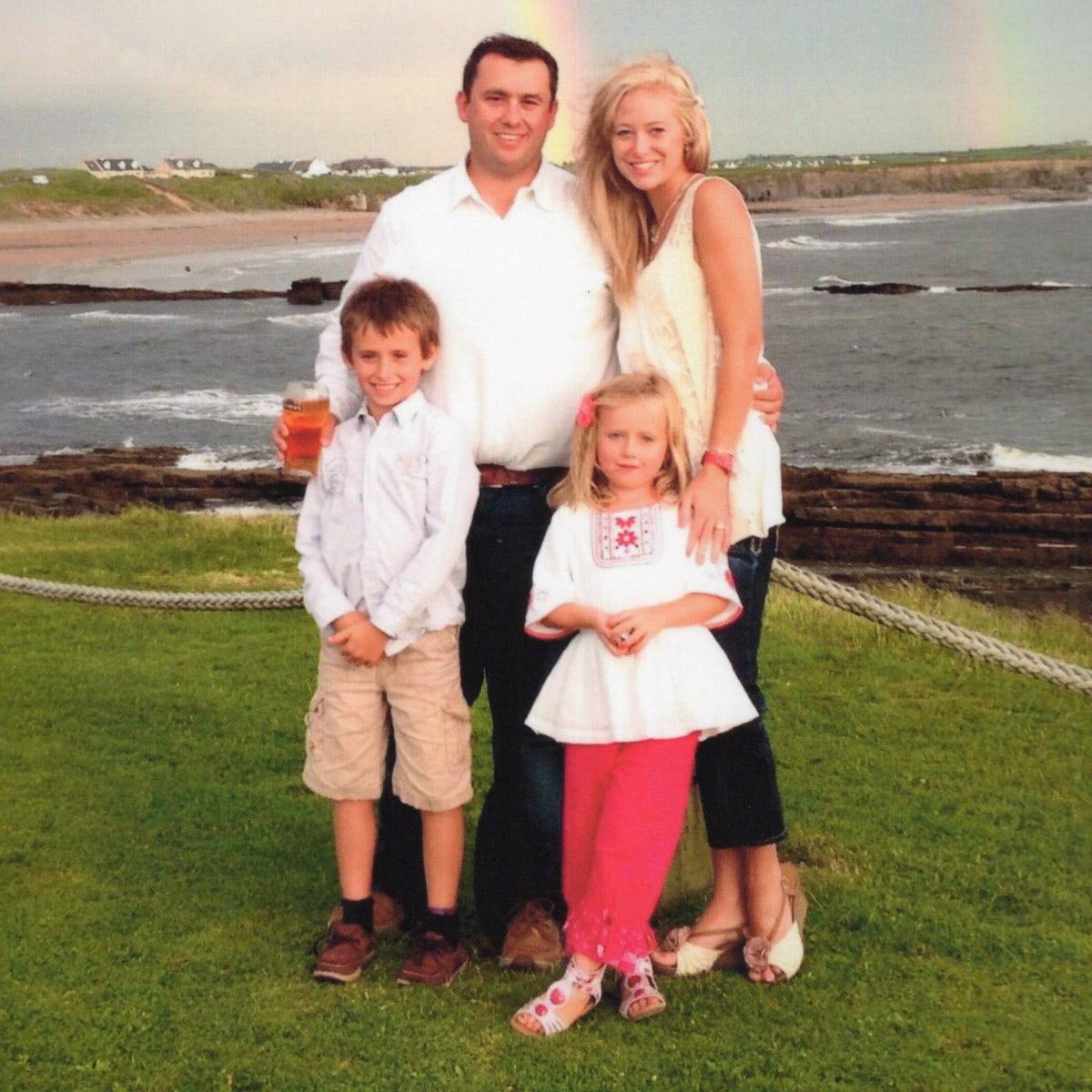Jason Corbett and Molly Martens with children Jack and Sarah family standing in front of the ocean with a rainbow in the sky