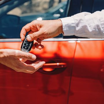 dealer giving car keys to the new owner close up of hands on the background of red automobile
