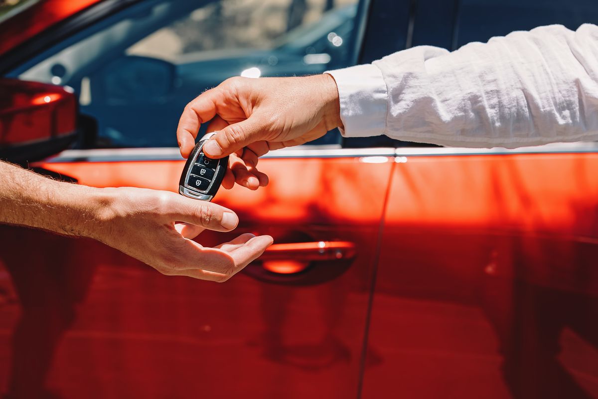 dealer giving car keys to the new owner close up of hands on the background of red automobile