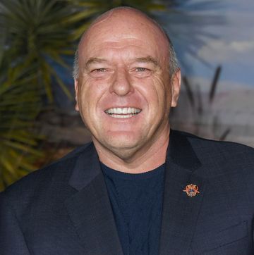 an older gentleman, balding with grey hair, smiling broadly at the camera, wearing a dark blue tshirt and suit jacket