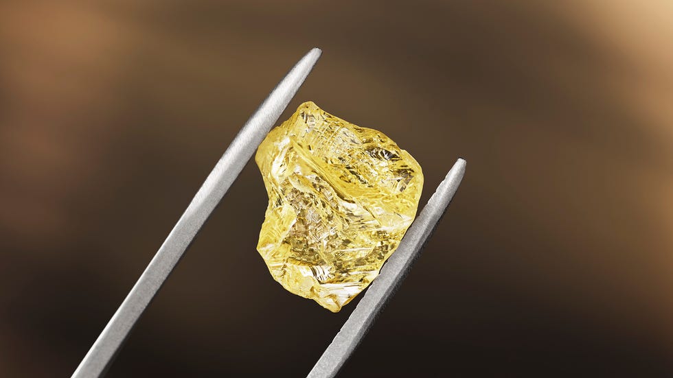 a rough yellow diamond being held up by metal tools