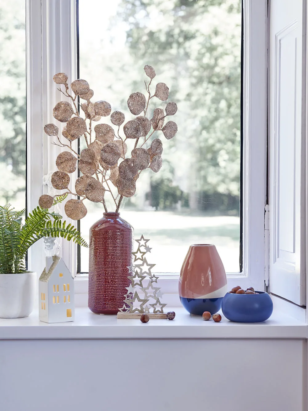 jarrones en ceramica roja y azul con ramas de hojas blancas junto a un ventanal