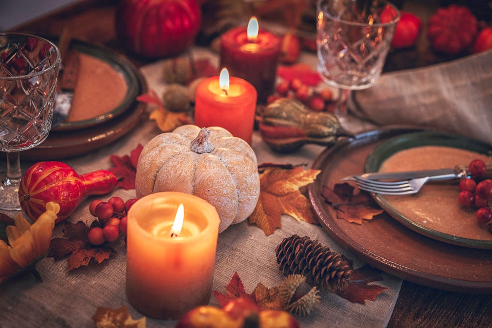 decorated table for thanksgiving dinner with candles, pumpkins, leafs and nuts