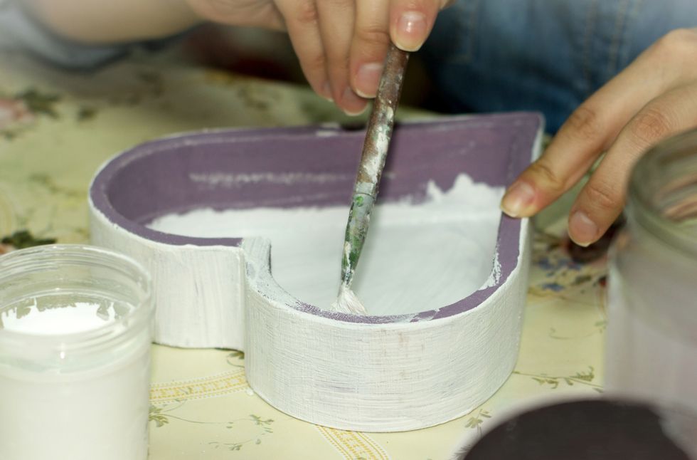 hands painting the inside of a purple wooden heart shaped box white