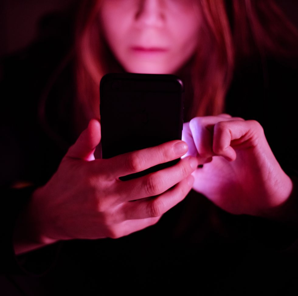 woman using her phone at night bathed in shadows and pink light