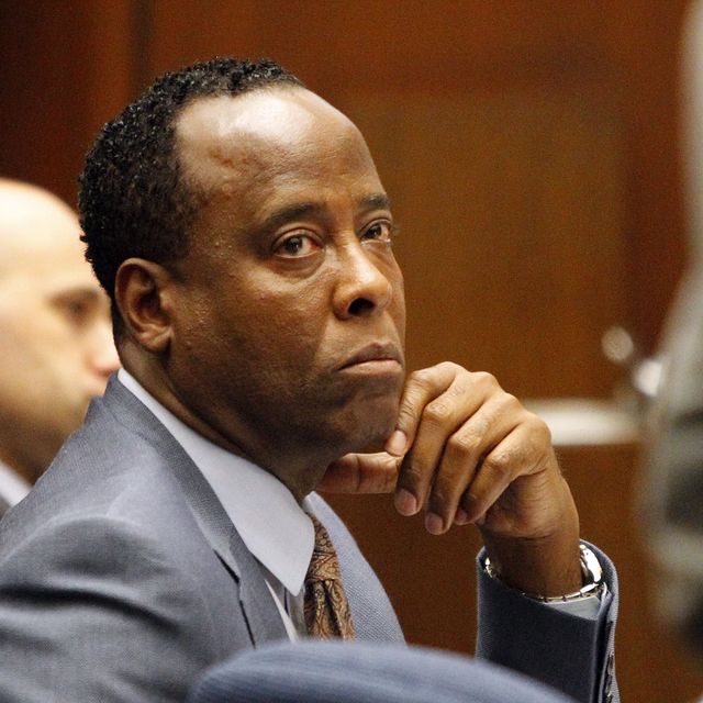 a man sits inside a room and looks up to the left, he wears a gray suit light collared shirt and tie