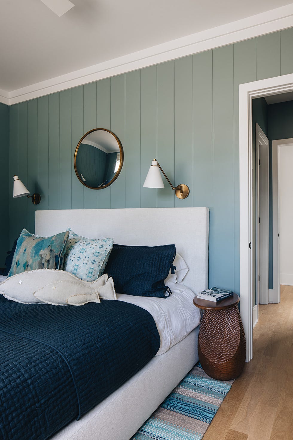 Modern bedroom with bluegreen walls a bed with decorative pillows and a round mirror