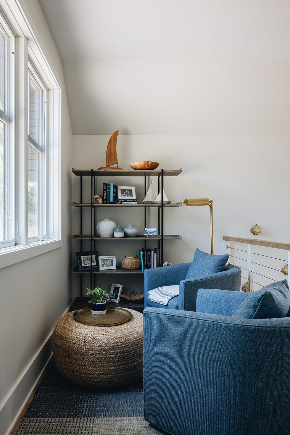 A cozy corner with two blue armchairs a natural fiber ottoman and a bookshelf