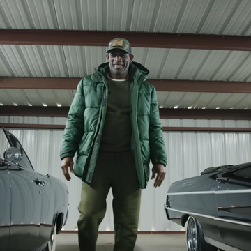 a man in a green coat and hat standing between two cars