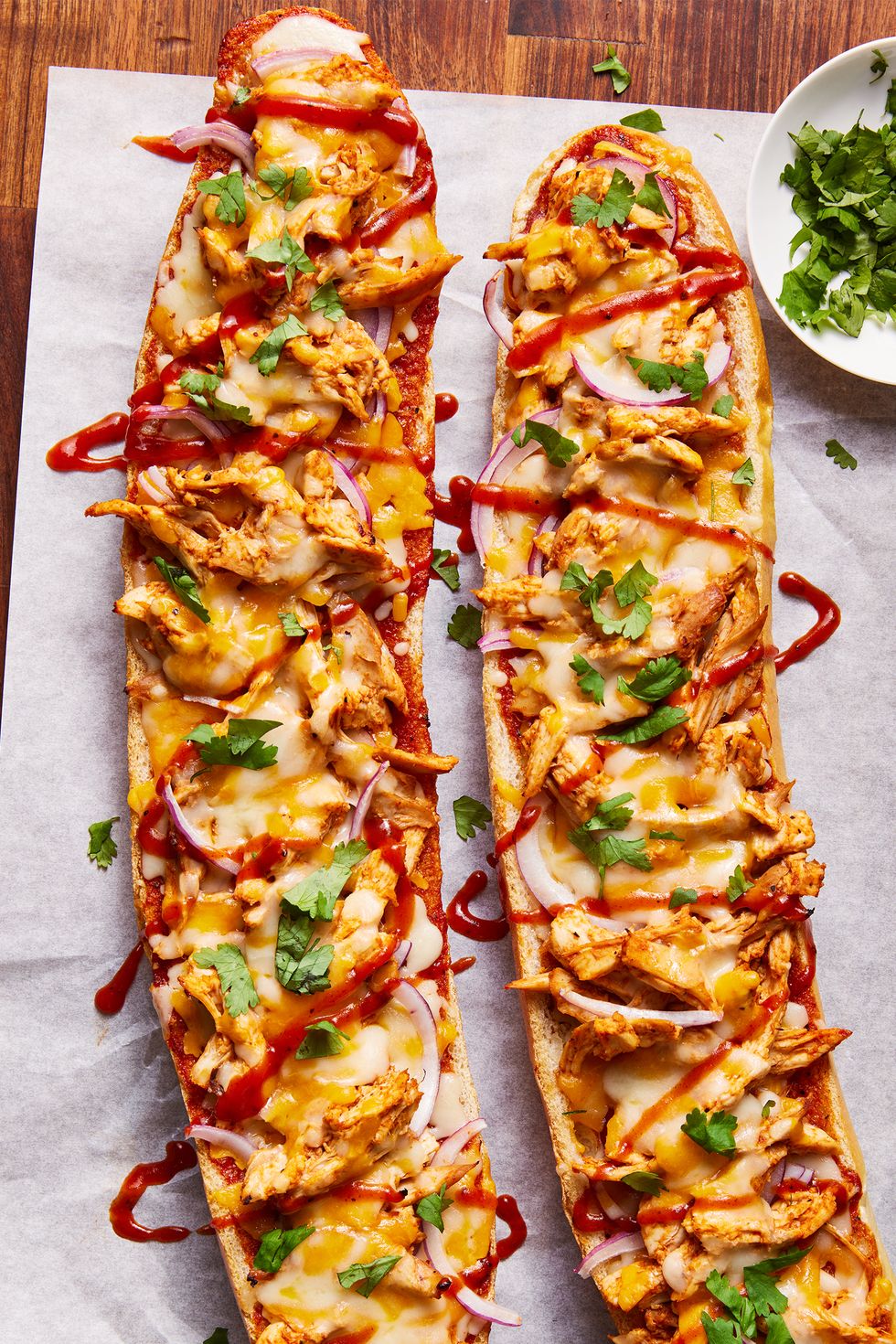 a loaf of french bread sliced in half and topped with shredded chicken, barbecue sauce, cheese, red onions, and cilantro