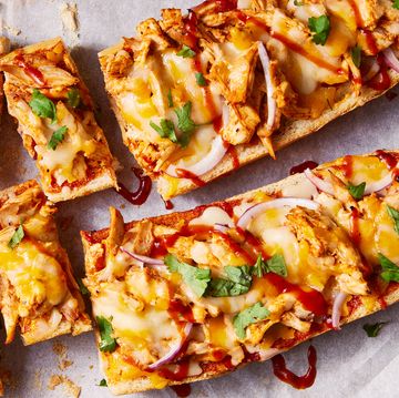 a loaf of french bread sliced in half and topped with shredded chicken, barbecue sauce, cheese, red onions, and cilantro