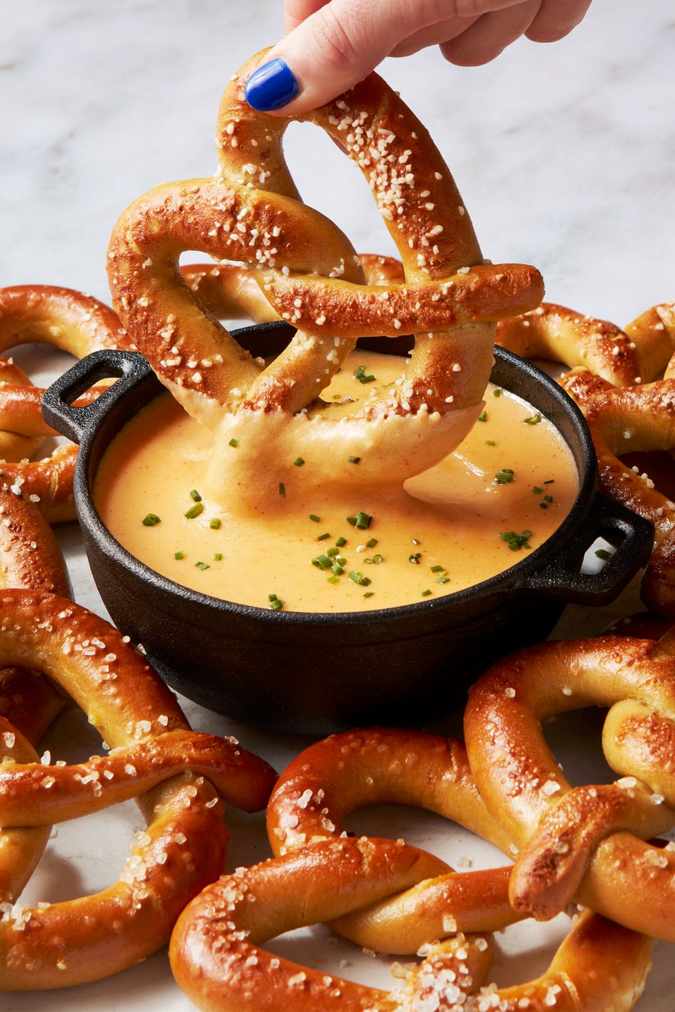 dipping a soft pretzel into a pot of beer cheese topped with chives