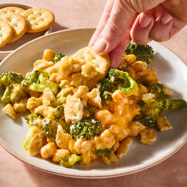 Cheesy broccoli cheddar chickpea skillet a hand dipping a ritz cracker into cheesy broccoli cheddar chickpeas