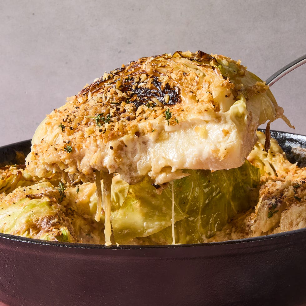 spoon lifting a wedge of french onion cabbage gratin from a cast iron pan