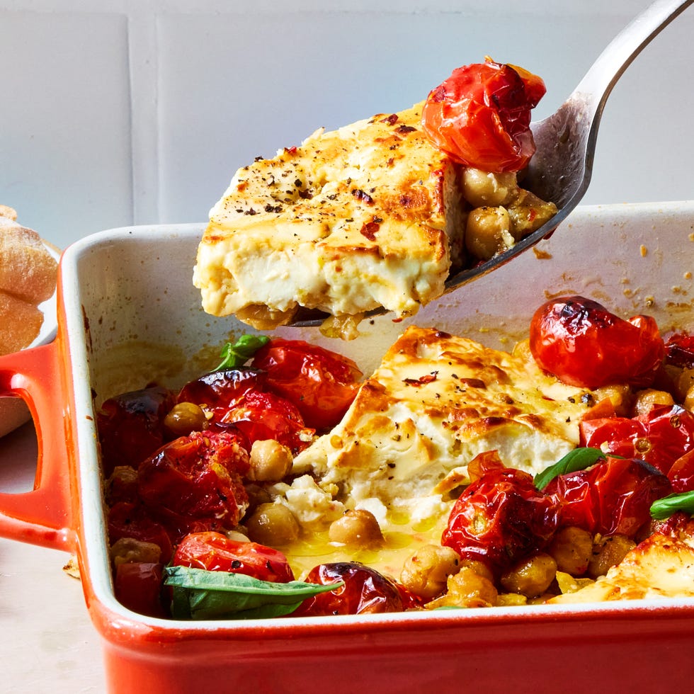 a spoon lifting baked feta, tomato, and chickpeas from a casserole dish