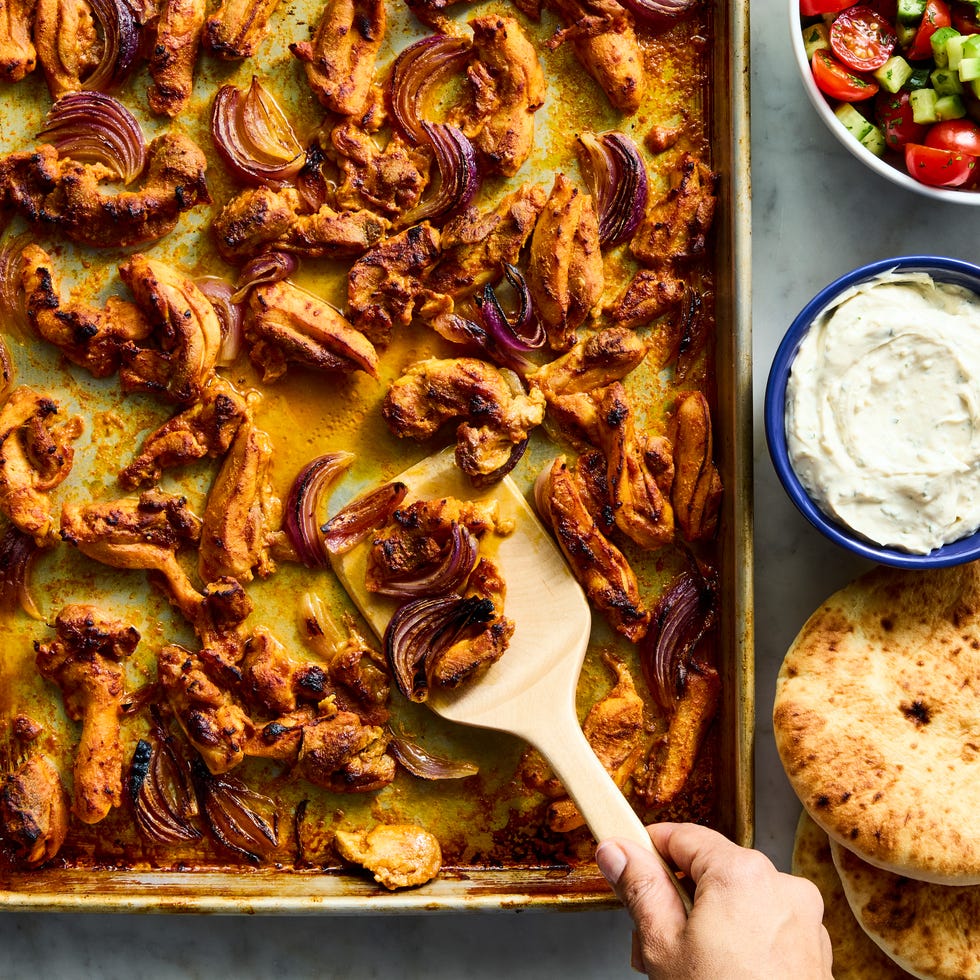 strips of chicken thigh are marinated in greek yogurt, cumin, coriander, and paprika, roasted on a sheet pan with red onion, then topped with a bright cucumber tomato salad and herby tahini yogurt dressing