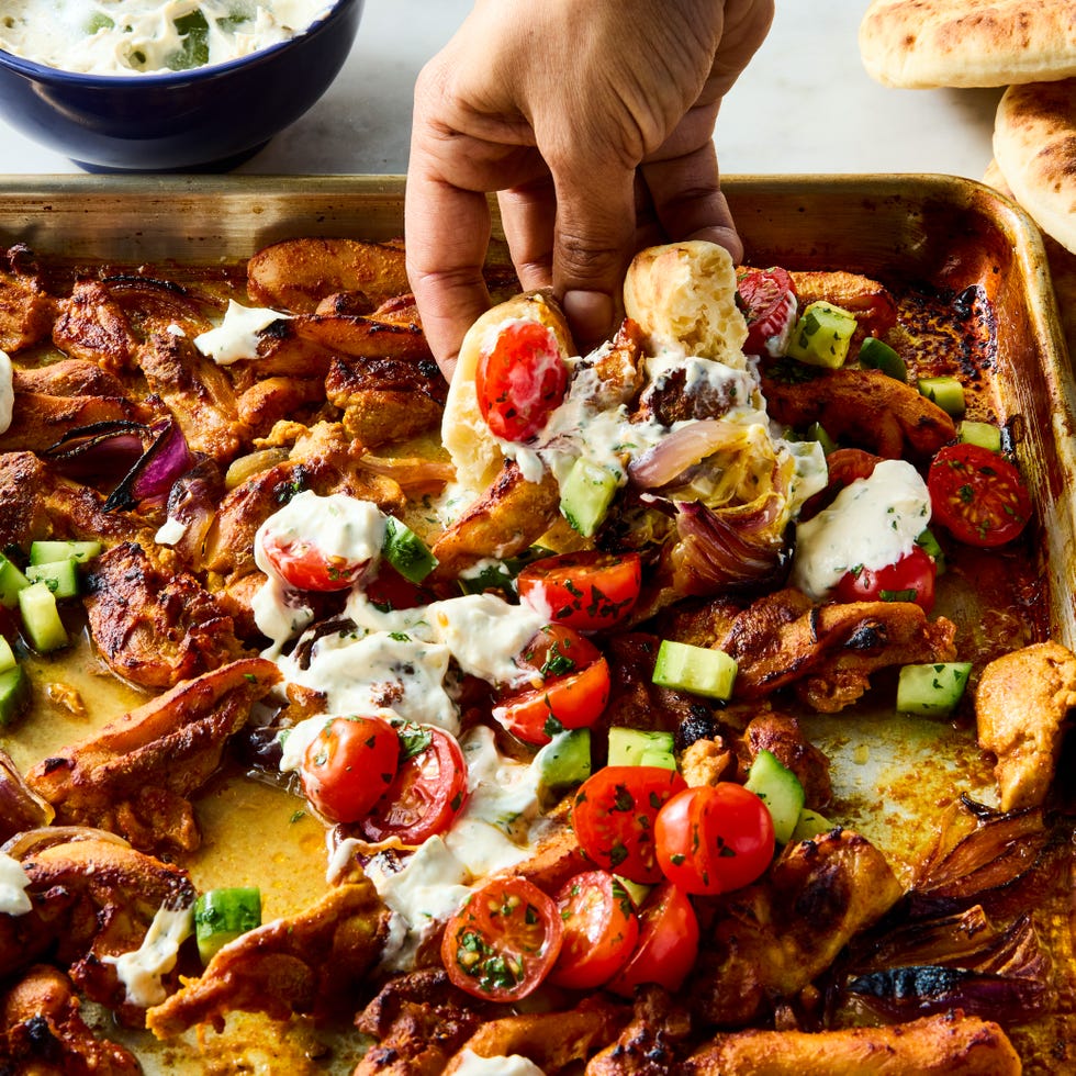 strips of chicken thigh are marinated in greek yogurt, cumin, coriander, and paprika, roasted on a sheet pan with red onion, then topped with a bright cucumber tomato salad and herby tahini yogurt dressing