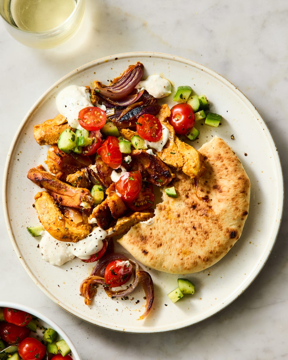 strips of chicken thigh are marinated in greek yogurt, cumin, coriander, and paprika, roasted on a sheet pan with red onion, then topped with a bright cucumber tomato salad and herby tahini yogurt dressing