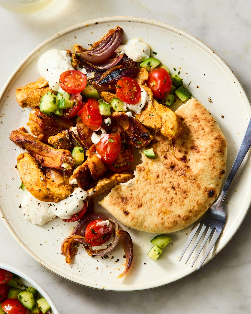 strips of chicken thigh are marinated in greek yogurt, cumin, coriander, and paprika, roasted on a sheet pan with red onion, then topped with a bright cucumber tomato salad and herby tahini yogurt dressing