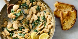 creamy lemon garlic butter beans in a pan with lemon slices and toast on the side