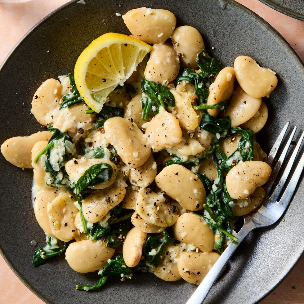 creamy lemon garlic butter beans on a plate with a wedge of lemon and a fork