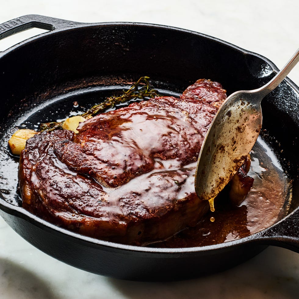 reverse sear steak in a cast iron pan with garlic and thyme being basted with butter