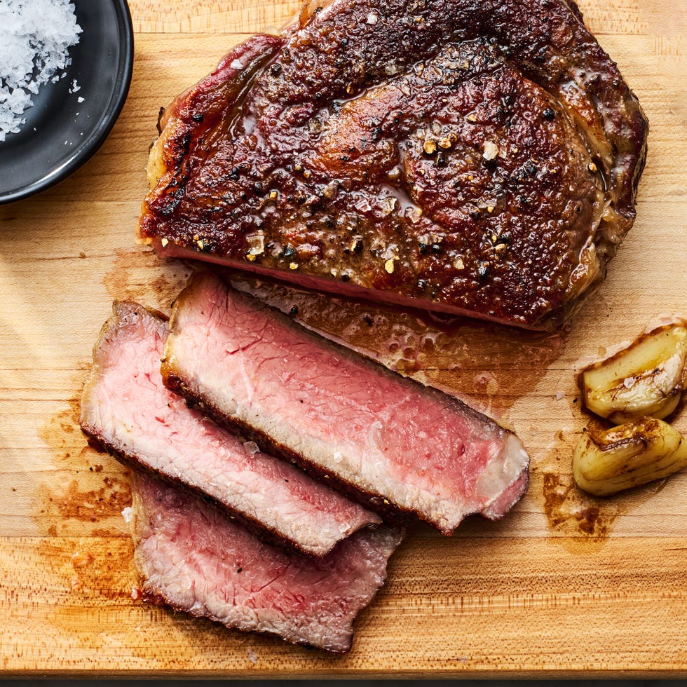 reverse sear steak sliced on a cutting board with a bowl of salt and garlic cloves