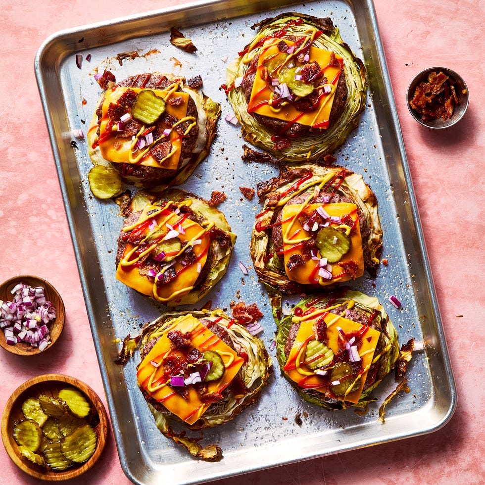 roasted cabbage burgers on a sheet pan topped with american cheese, bacon, red onion, pickles, ketchup, and mustard