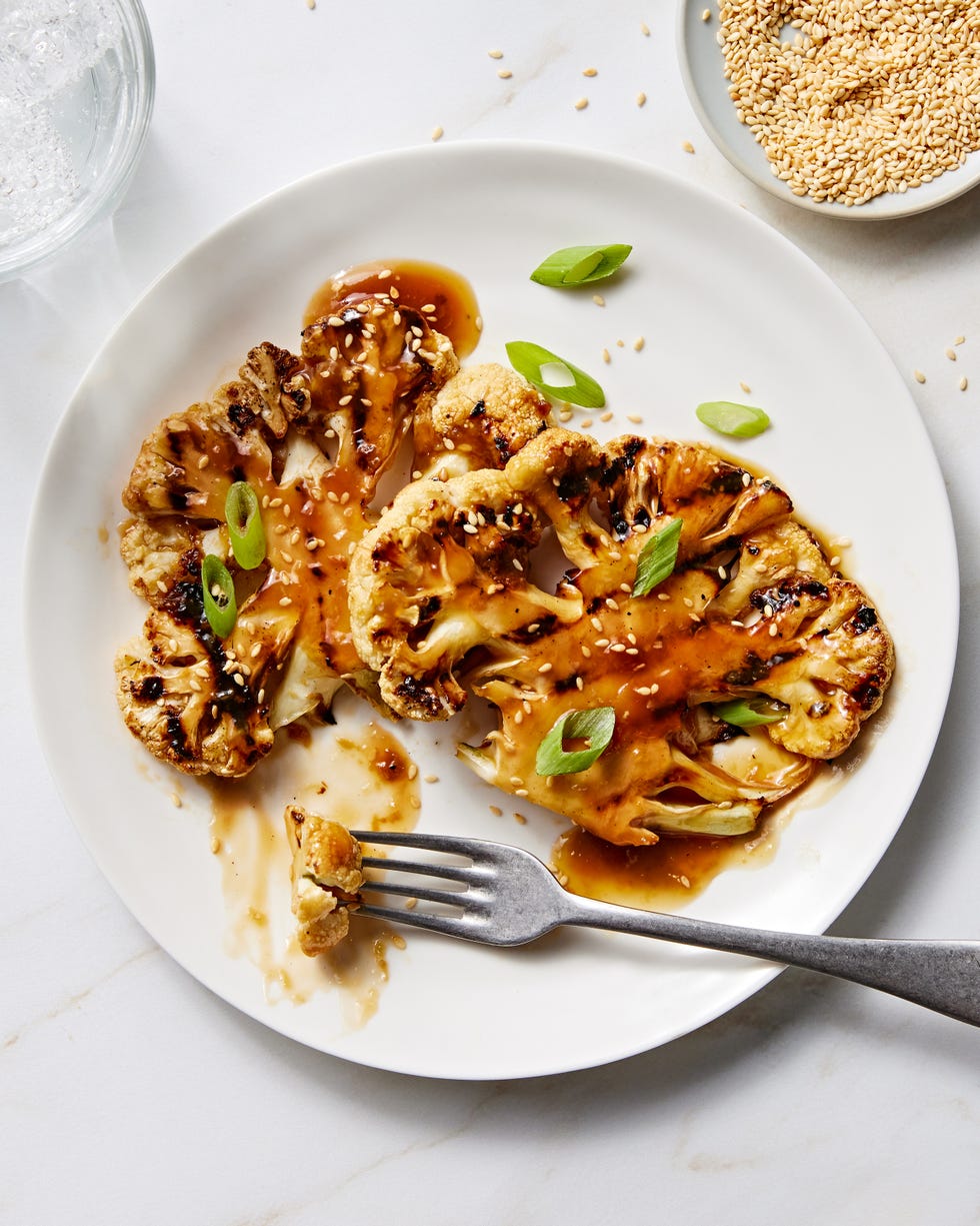 grilled teriyaki cauliflower steaks on a white plate topped with sesame seeds and scallions