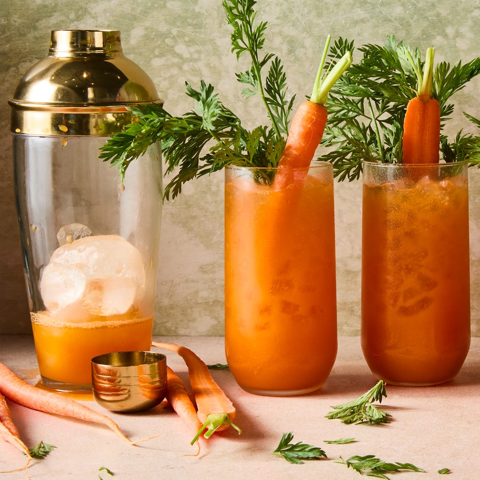 orange carrot margaritas in a tall glass with carrots and carrot stems as garnish