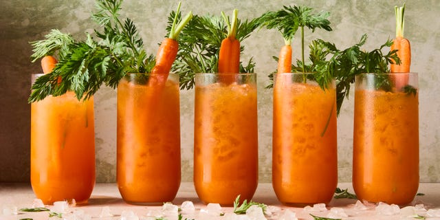 orange carrot margaritas in a tall glass with carrots and carrot stems as garnish
