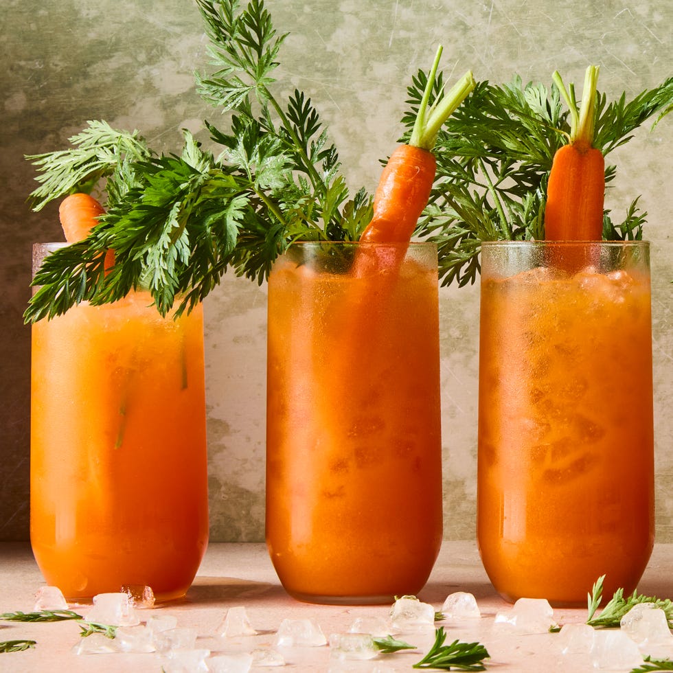 orange carrot margaritas in a tall glass with carrots and carrot stems as garnish