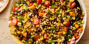 a bowl with pearl couscous, black beans, corn, bell peppers, cherry tomatoes, scallions, cilantro, and pickled jalapenos