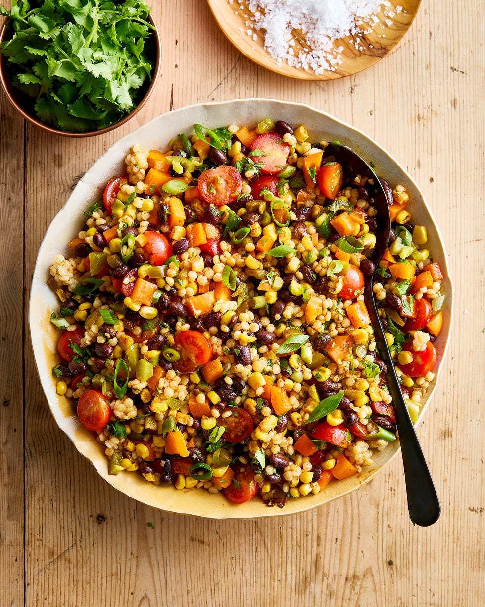 a bowl with pearl couscous, black beans, corn, bell peppers, cherry tomatoes, scallions, cilantro, and pickled jalapenos