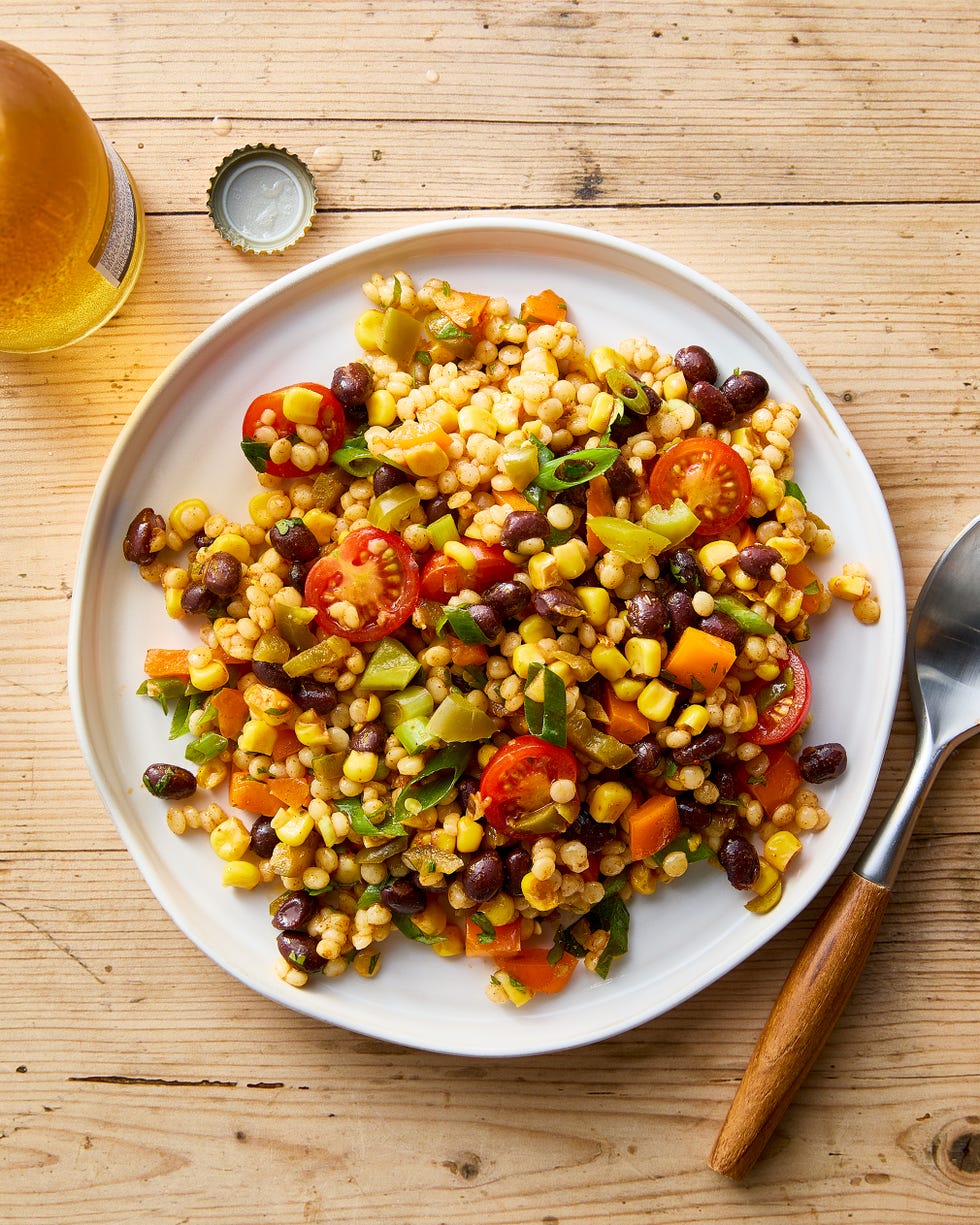a bowl with pearl couscous, black beans, corn, bell peppers, cherry tomatoes, scallions, cilantro, and pickled jalapenos