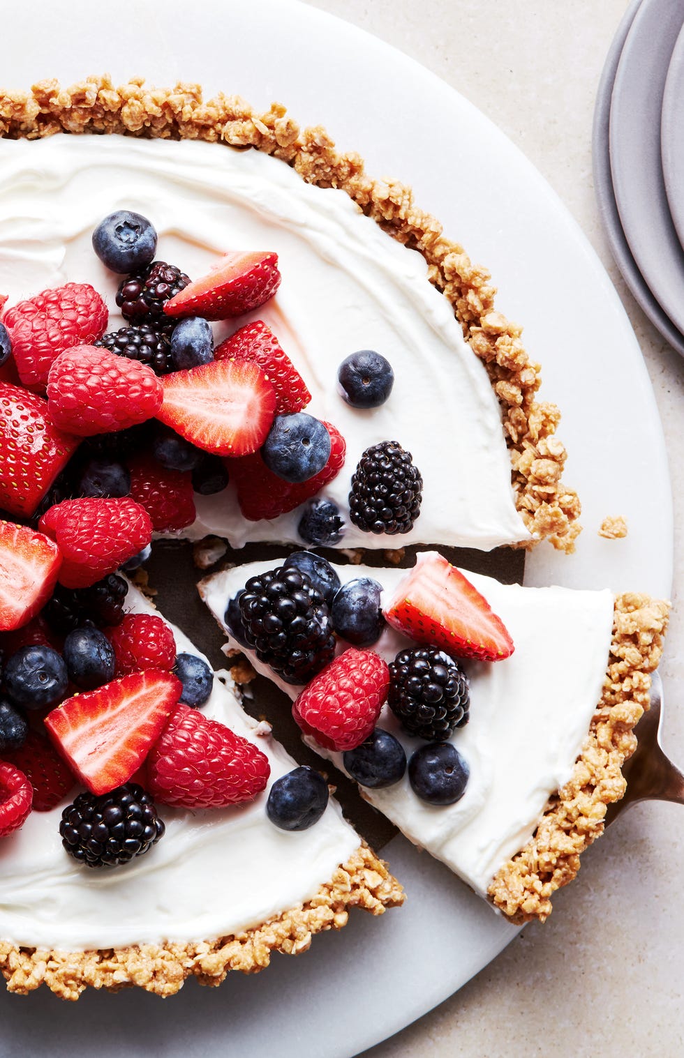 a slice of no bake fruit and granola breakfast tart coming out of the larger tart, topped with blueberries, blackberries, raspberries, and strawberries