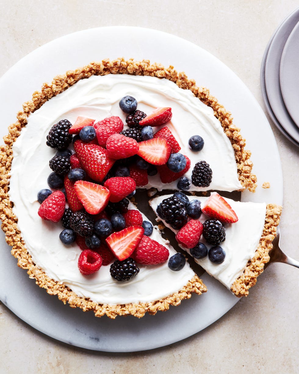 a slice of no bake fruit and granola breakfast tart coming out of the larger tart, topped with blueberries, blackberries, raspberries, and strawberries